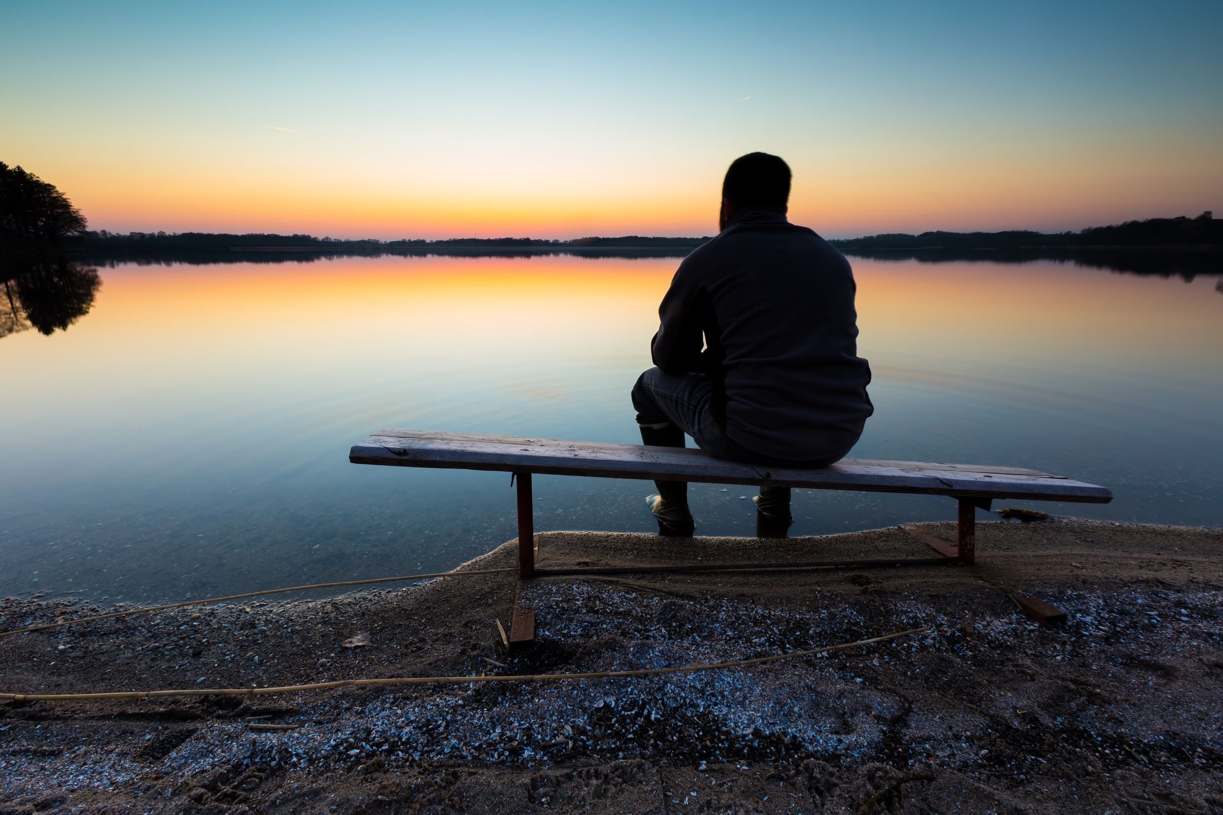 Грустное озеро. Одинокий человек на скамейке. Человек сидит на причале. Человек на берегу озера. Мужчина сидит на берегу реки.